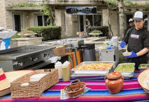 A catering setup with a flat grill, tables with festiv cloth, an employee preparing some Mexican food